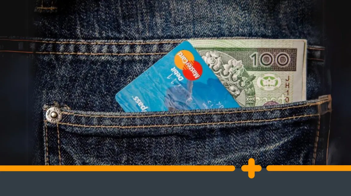 Karta debetowa Mastercard i banknot 100 zł wystające z kieszeni jeansów